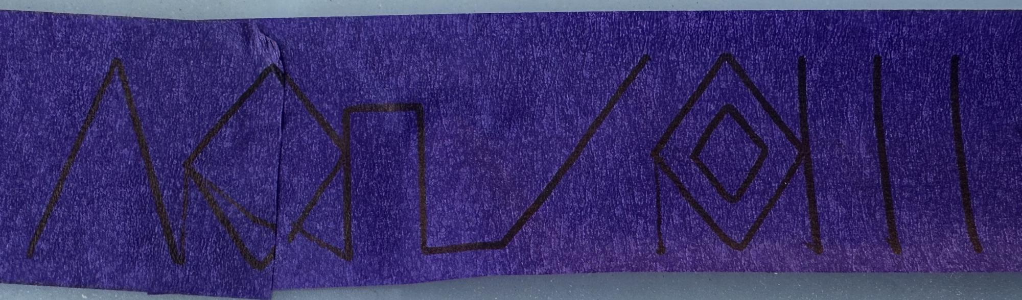 A strip of purple label tape inked in black with a row of geometric Aztec
motifs — a chevron, a battlement, a cross, a nested diamond and vertical
bars.